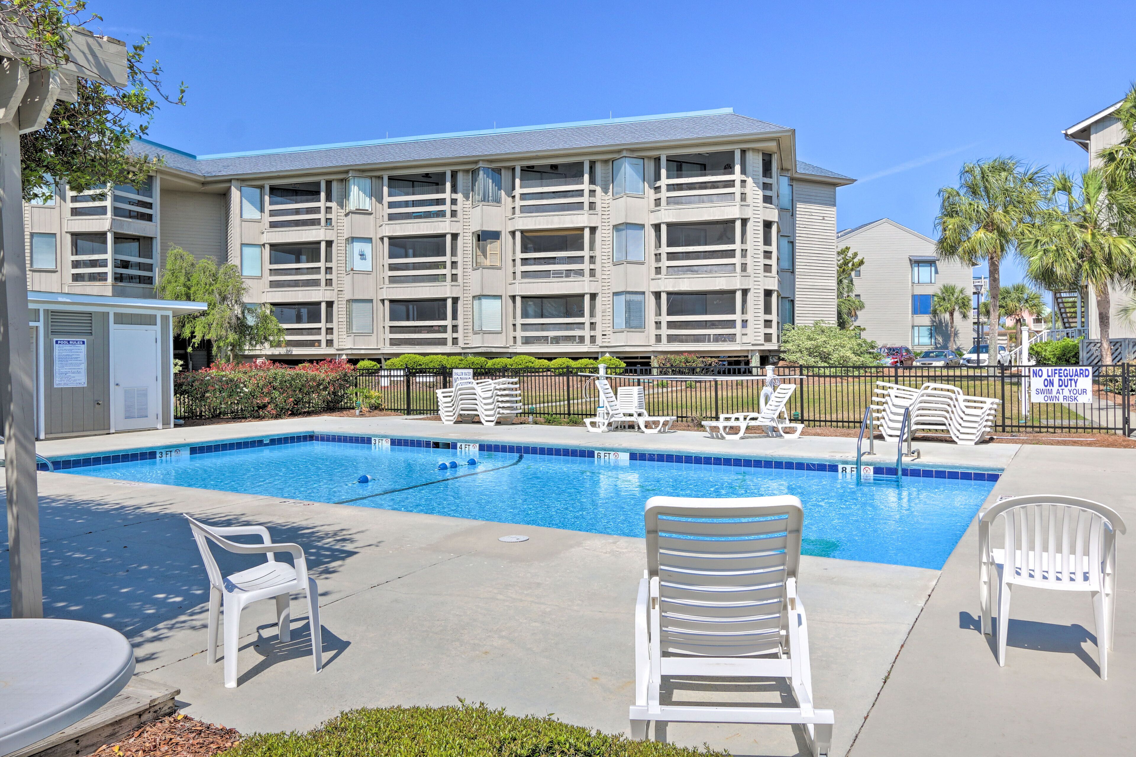 A swimming pool with white lounge chairs, a lifeguard station, and a multi-story building with balconies.
