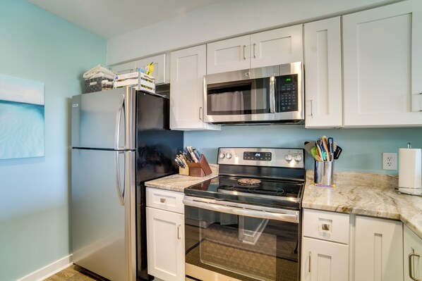 A kitchen with white cabinets, a stainless steel refrigerator, a microwave, a stove, and a sink. - Pool Access & Views at Saint Helena Island Condo! (Harbor Island)