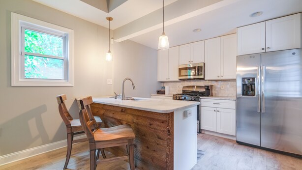 A modern kitchen with white cabinets, stainless steel appliances, and a wooden island with chairs.