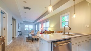 A modern kitchen with a central island, built-in dishwasher, and a large window providing natural light.