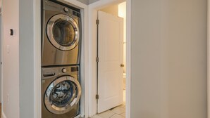 A laundry room with two stacked front-loading washing machines and a white door leading to another room.