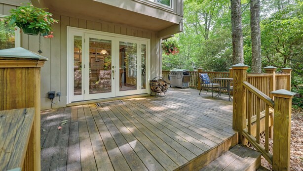 A wooden deck with a covered patio area, outdoor furniture, and a view of the surrounding forest.