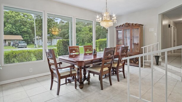 A dining area with a large table and chairs, a chandelier, and a view of the outside.