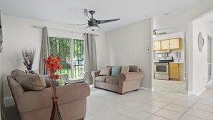 A living room with two sofas, a ceiling fan, and a view to the kitchen.