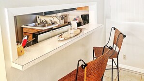A kitchen with a built-in island, two wicker chairs, a mirror, and a window.