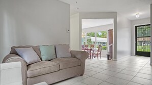 A living room with a beige sofa, a small table, and a view of a patio area with outdoor furniture.