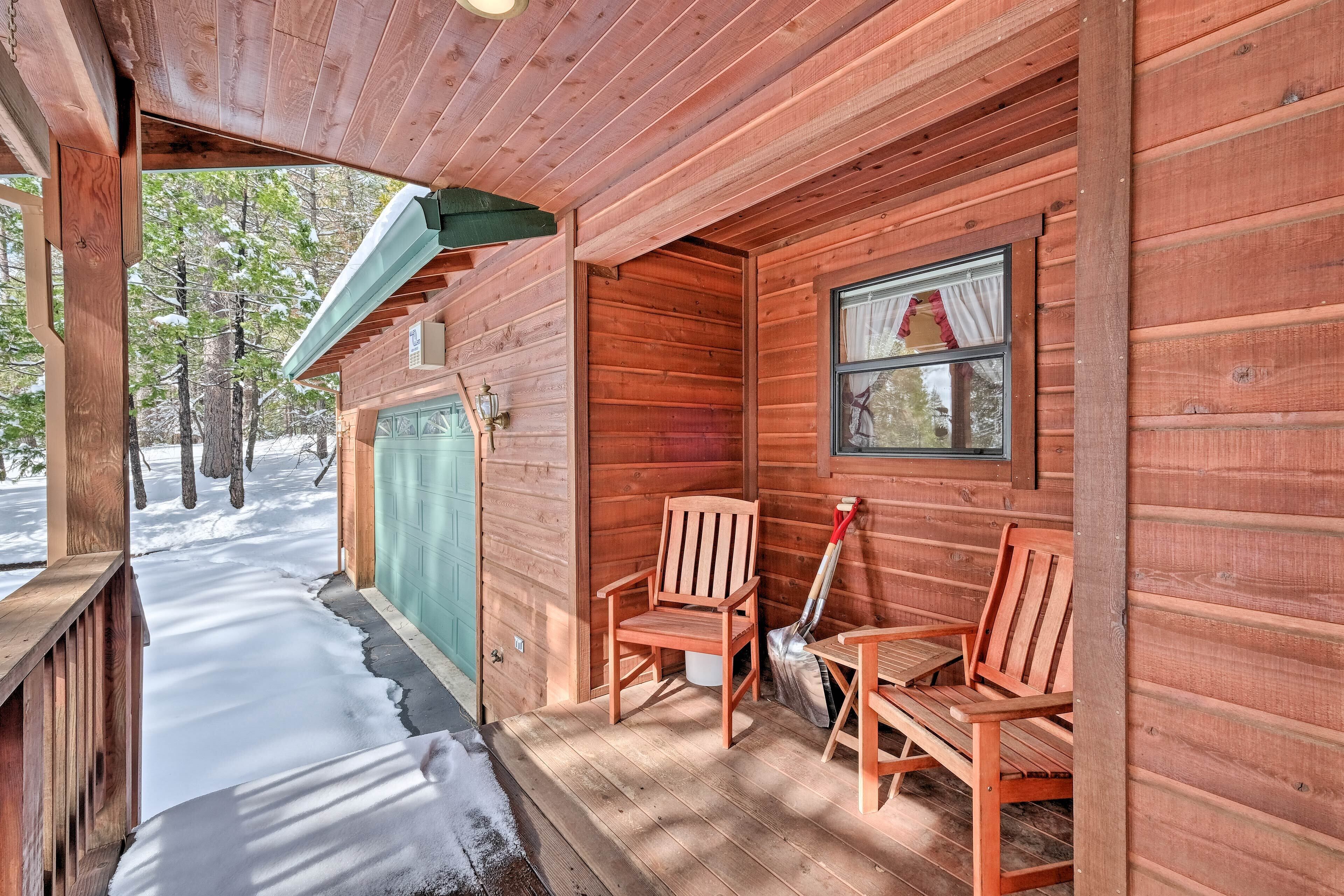 Een houten chalet met een veranda, twee houten stoelen, een tafel en een raam met gordijnen.