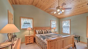 A bedroom with a wooden bed, two bedside tables with lamps, a ceiling fan, and windows with curtains. - Near Bear Valley: Peaceful Arnold Home w/ Hot Tub (Arnold)