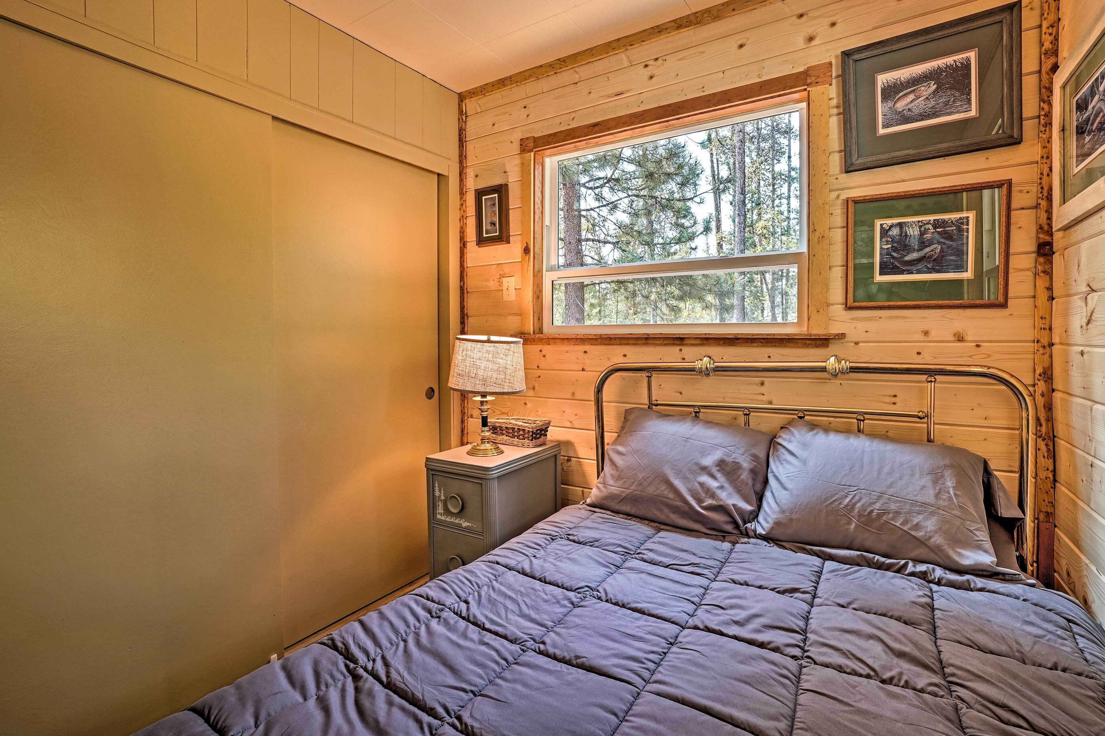 A wooden cabin bedroom with a bed, nightstand, lamp, and framed pictures on the wall.