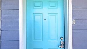 Une porte bleue dotée d’un clavier de code, encadrée de blanc, sur un mur recouvert de bardage gris.