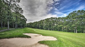 A golf course with sand bunkers, well-maintained grass, and a dense forest in the background.