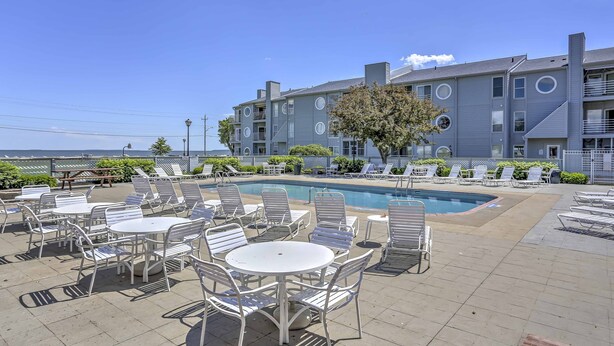 A poolside area with lounge chairs and tables, a pool, and a building with balconies. - Charming Port Clinton Condo w/ Community Amenities (Port Clinton)