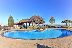 A swimming pool with a brick deck, surrounded by trees and a building with a red roof. - The Shores Condo w/ Beach Access < 2 Mi to Dtwn! (Port Clinton)
