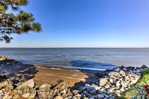 Een strand met een rotsachtige kustlijn, helderblauwe lucht en rustig water.