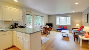 A spacious living area with a dining table, sofa, and a kitchen with white cabinets and a built-in island. - Central 4-acre Cottage w/ Deck: Walk to Bay! (Bainbridge Island)