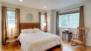 A neatly arranged bedroom with a large bed, bedside tables, a rocking chair, and a small table with a lamp. - Central 4-acre Cottage w/ Deck: Walk to Bay! (Bainbridge Island)