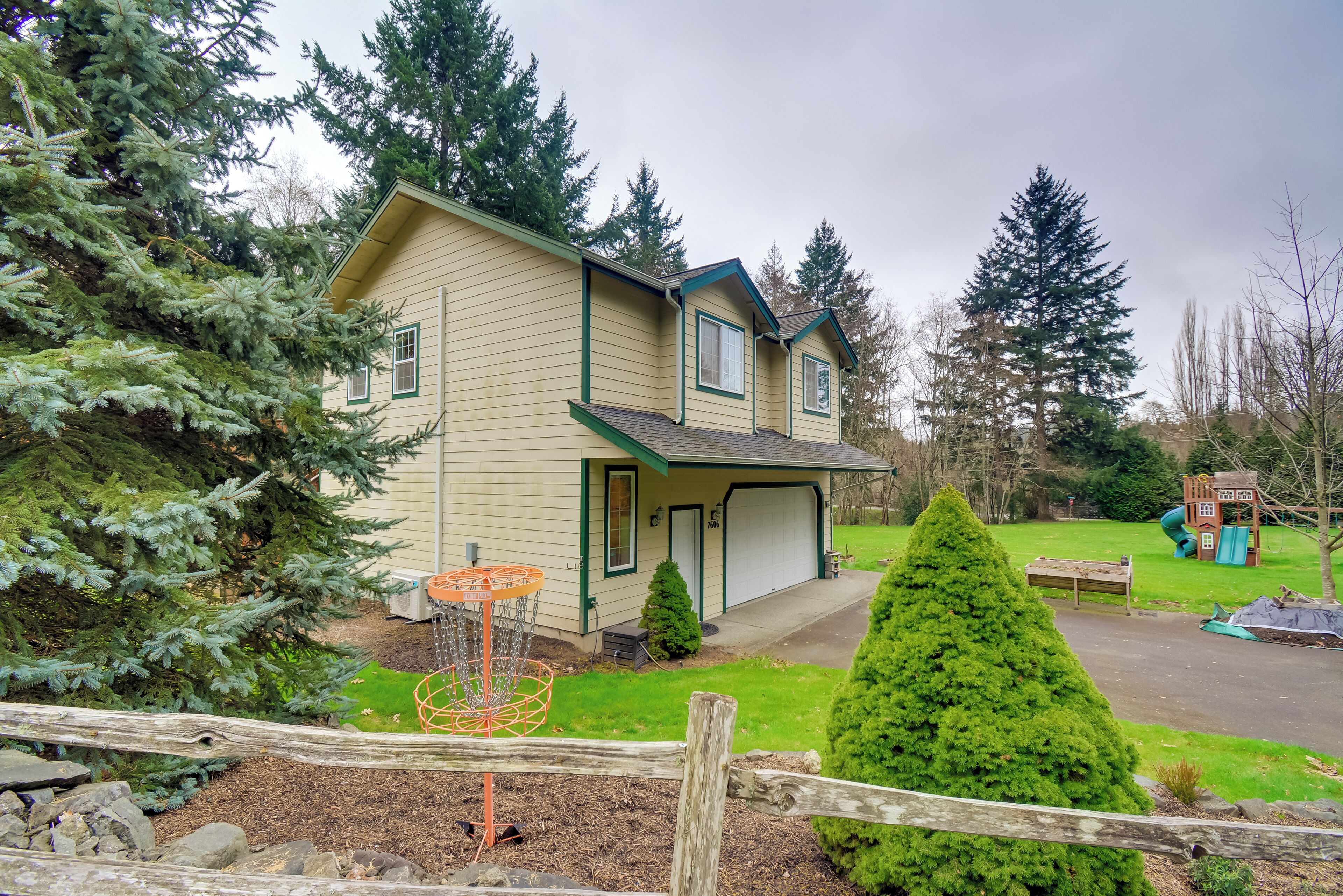 A two-story house with a garage, surrounded by evergreen trees and a well-maintained lawn.