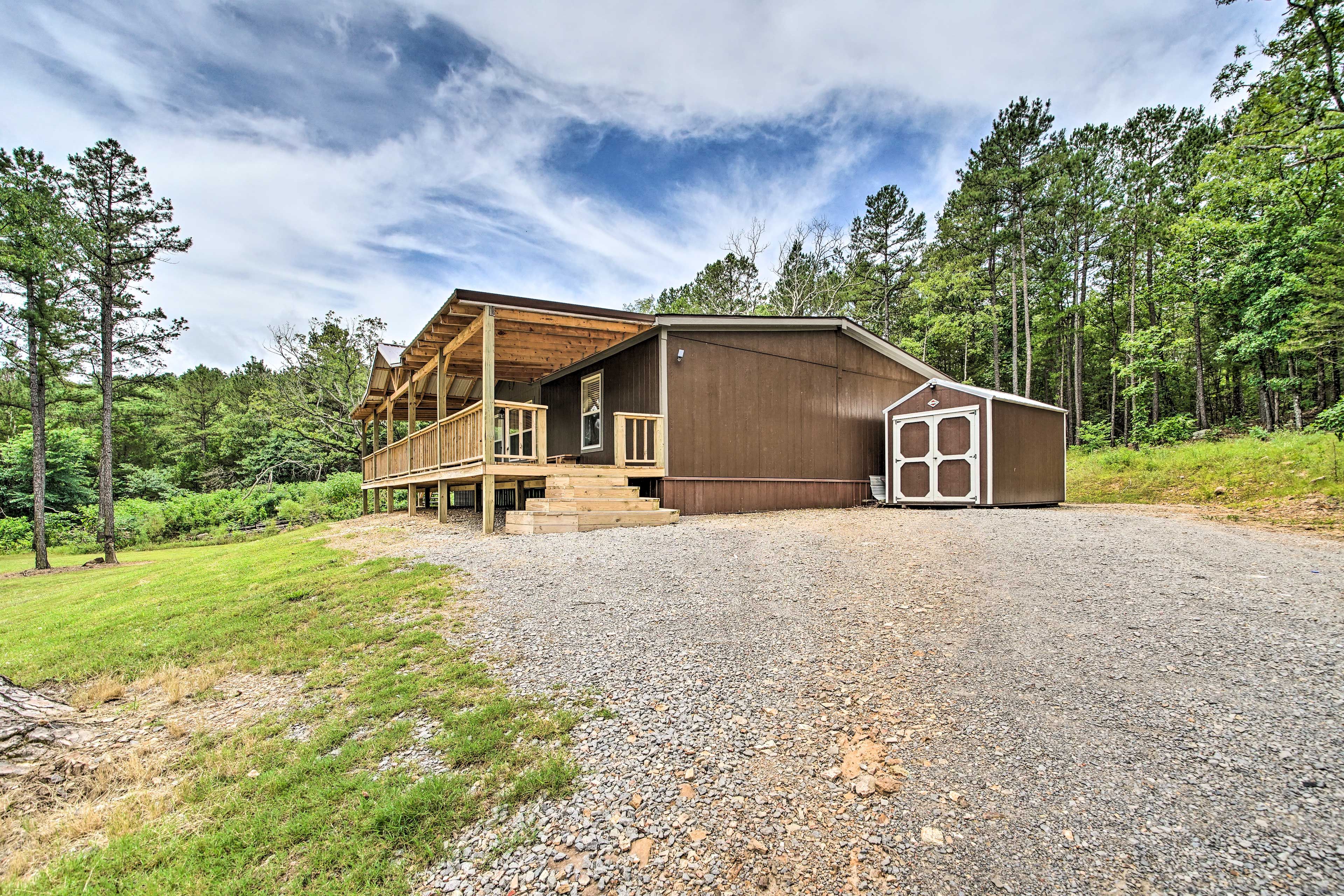 A rustic cabin with a wooden deck, a covered porch, and a gravel driveway.