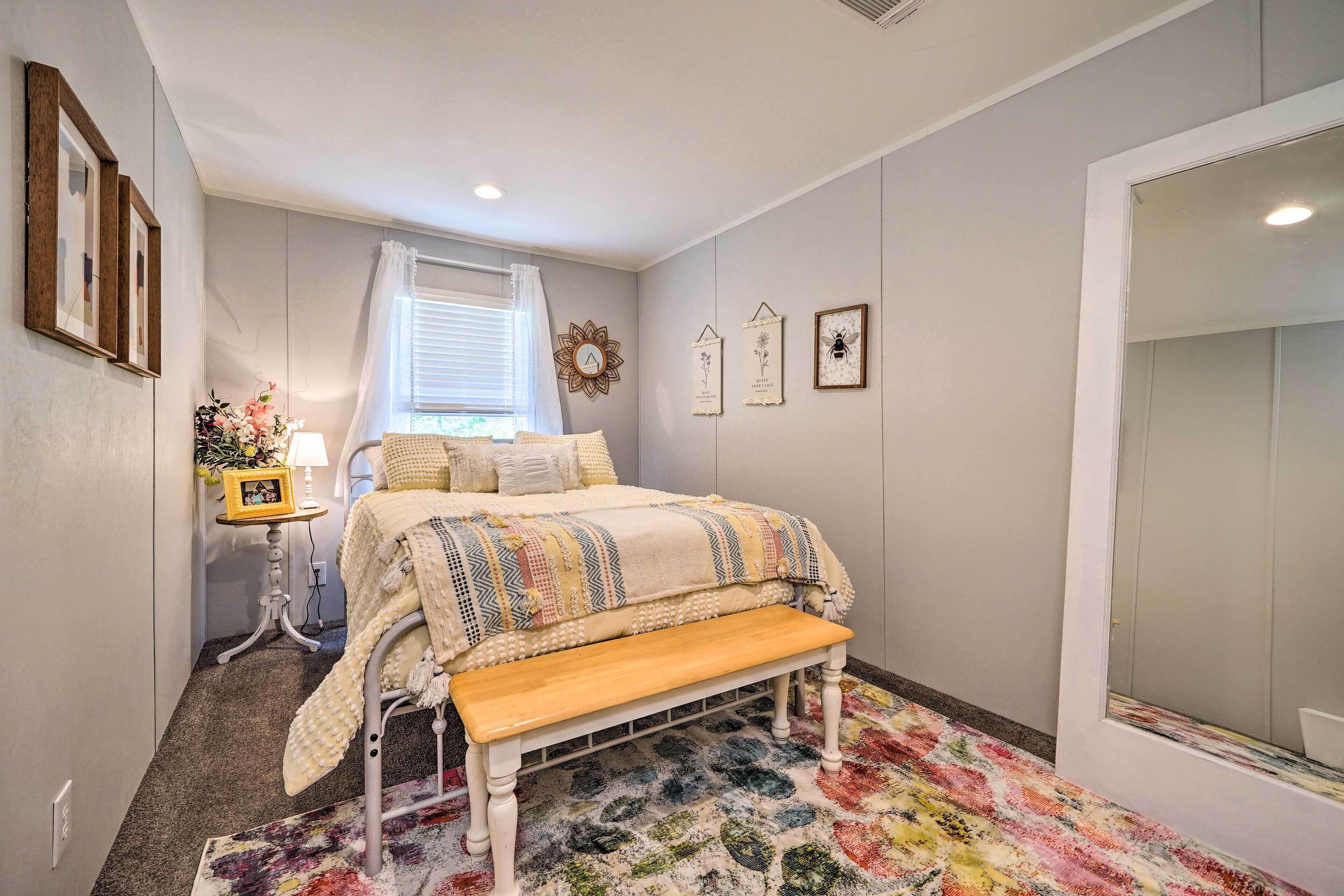A bedroom with a bed, a bench, a nightstand, a window with curtains, and wall decorations.