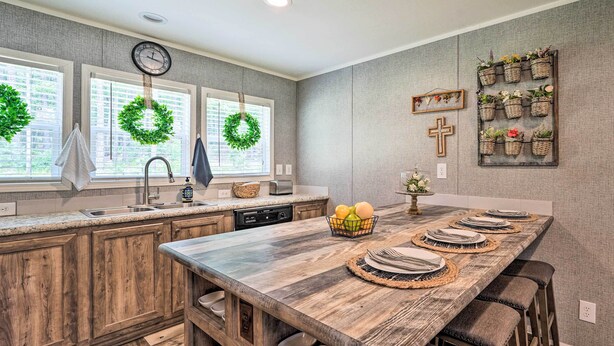 Una cocina con armarios de madera, una isla grande con taburetes de bar, un fregadero y una ventana decorada con un adorno.