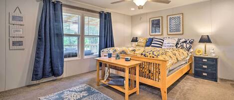 A bedroom with a bed, a nightstand, a table, a ceiling fan, and a window with curtains.