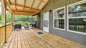 Una terraza techada con piso de madera, dos sillas de mimbre, una mesita y una puerta.