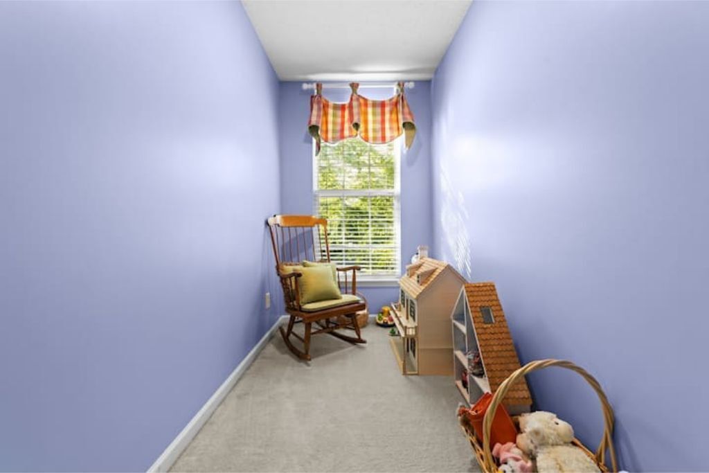 A room with a rocking chair, a small bookshelf, and a window with blinds.