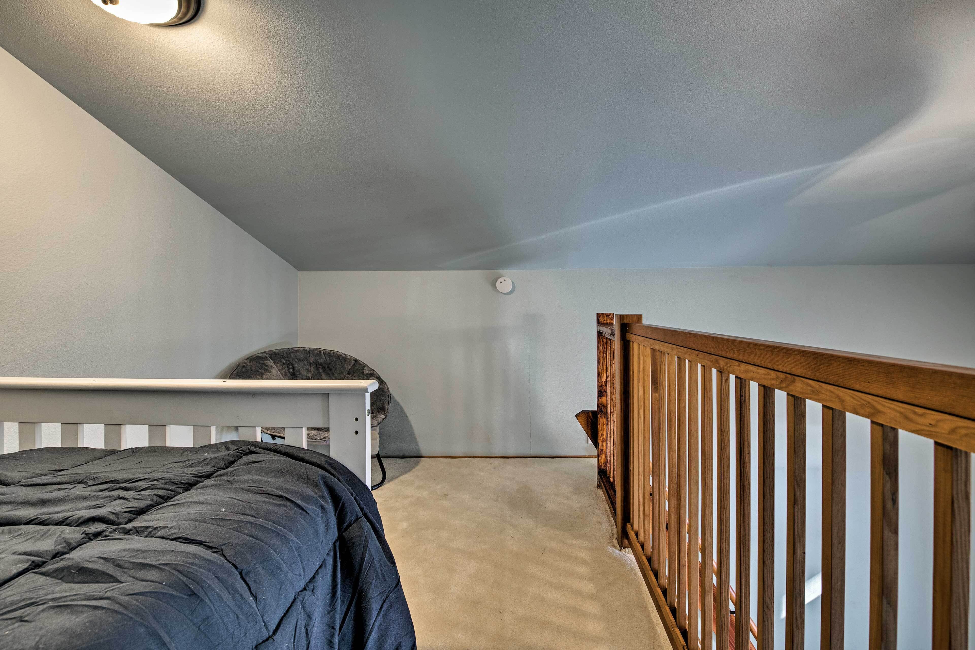 A bedroom with a single bed, a white headboard, a wooden railing, and a ceiling light.