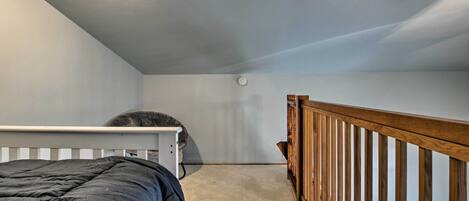 A bedroom with a single bed, a white headboard, a wooden railing, and a ceiling light.