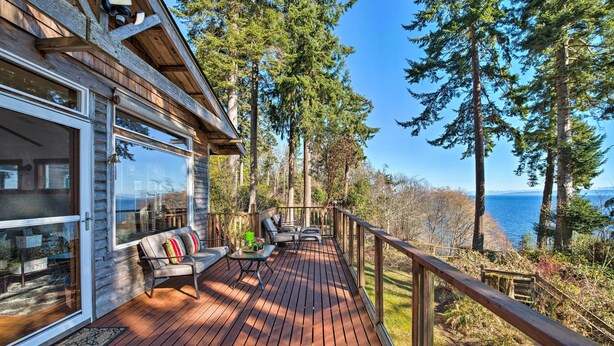 Una terraza de madera con un sofá y una mesa, con vistas a un bosque y el océano.