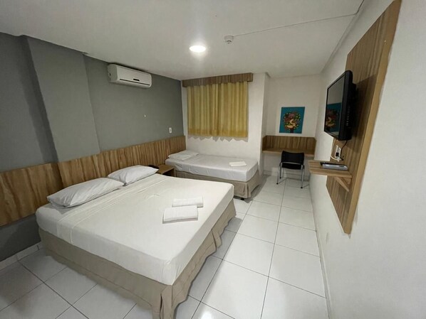 A hotel room with two beds, a TV, a small desk, and a window with curtains.