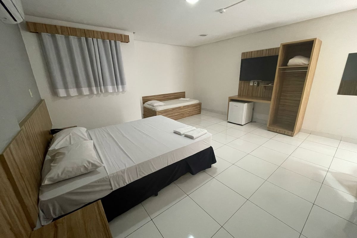 Une chambre d’hôtel moderne équipée d’un lit, d’un petit bureau, d’une armoire et d’une kitchenette compacte.