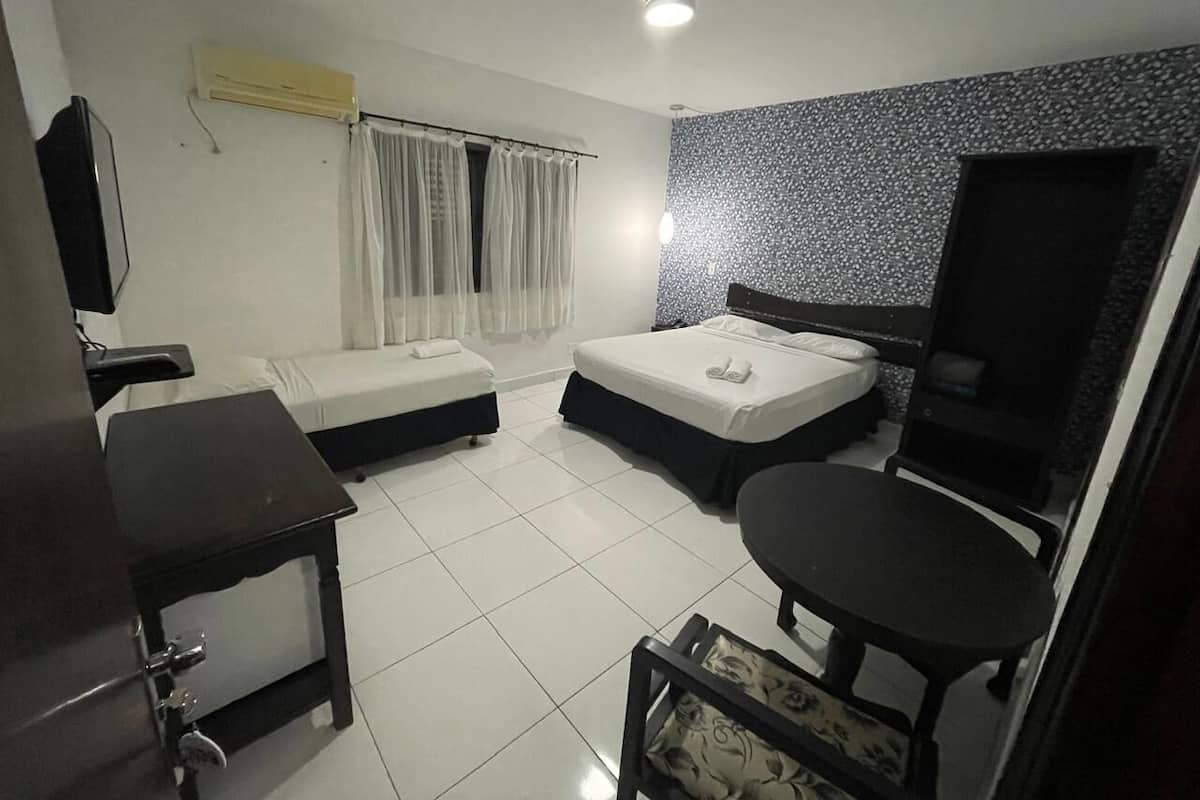 Une chambre d’hôtel de taille modeste, équipée de deux lits simples, d’une petite table, d’un téléviseur et d’une fenêtre avec des rideaux.
