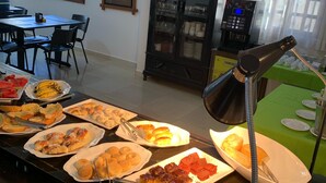 Montaje de bufé con diversos alimentos, un área de comedor con sillas y una mesa, y una cocina con cafetera.