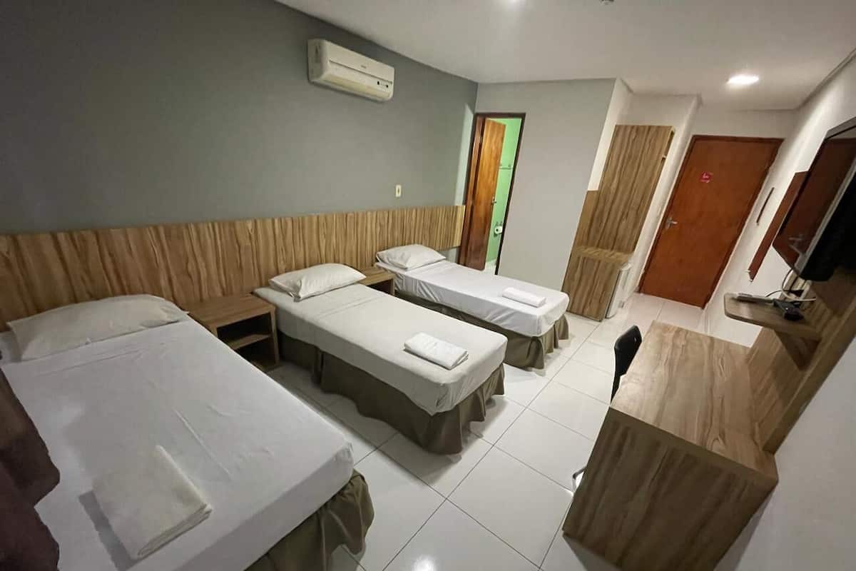Une chambre d’hôtel avec trois lits simples, une tête de lit en bois, une petite table et une armoire en bois.