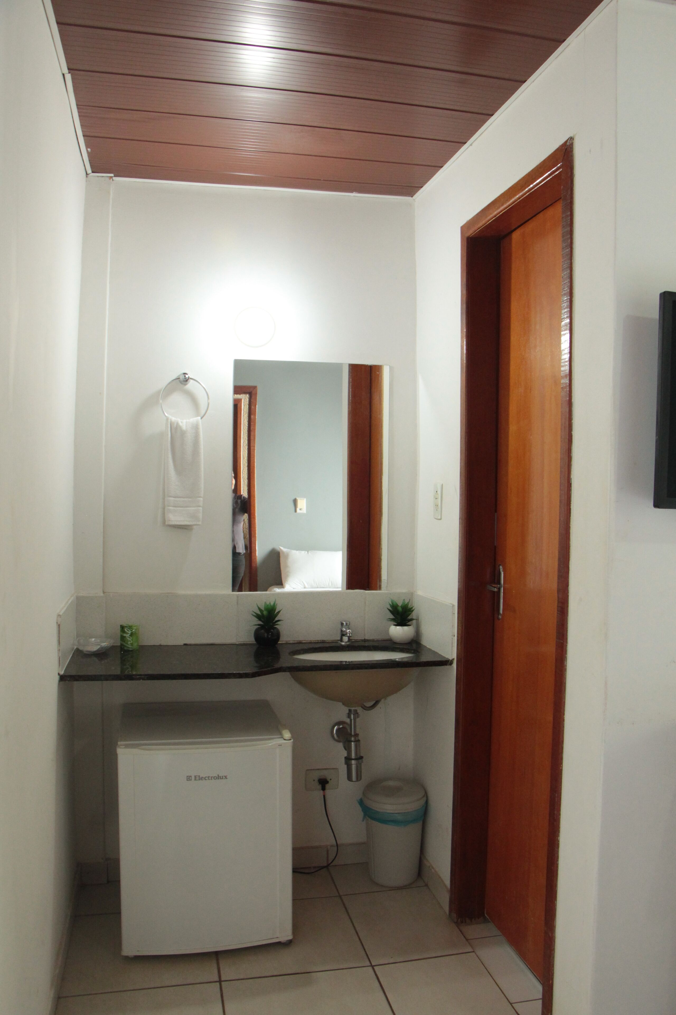 Un bagno piccolo con un frigorifero bianco, un lavandino, uno specchio e una porta in legno.