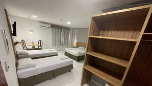 Habitación de hotel con dos camas individuales, un armario de madera, una mesita con sillas y un escritorio con lámpara.