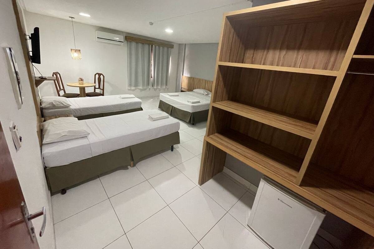 Une chambre d’hôtel avec deux lits simples, une armoire en bois, une petite table avec des chaises et un bureau avec une lampe.