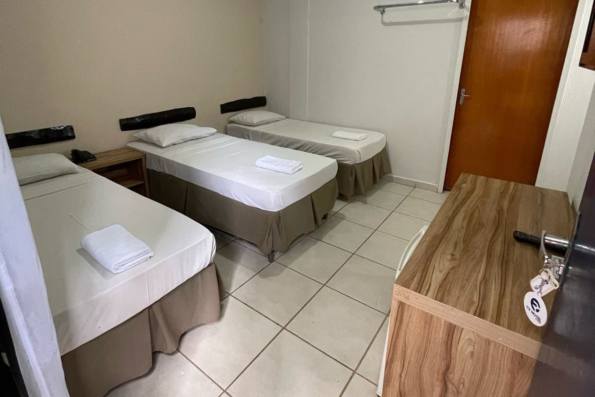 Une petite pièce propre, avec deux lits simples, un bureau en bois, un miroir et une porte.