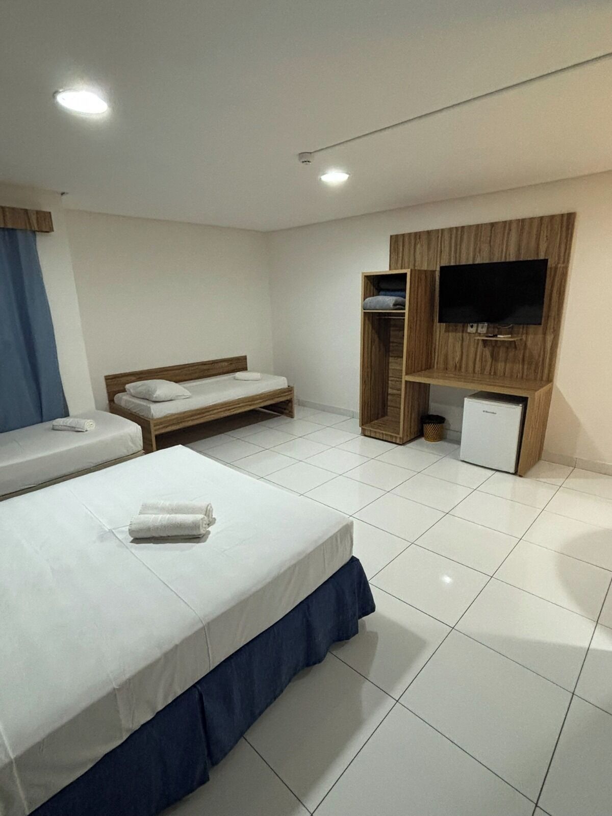 A hotel room with two beds, a TV, a small fridge, and a wooden wardrobe.