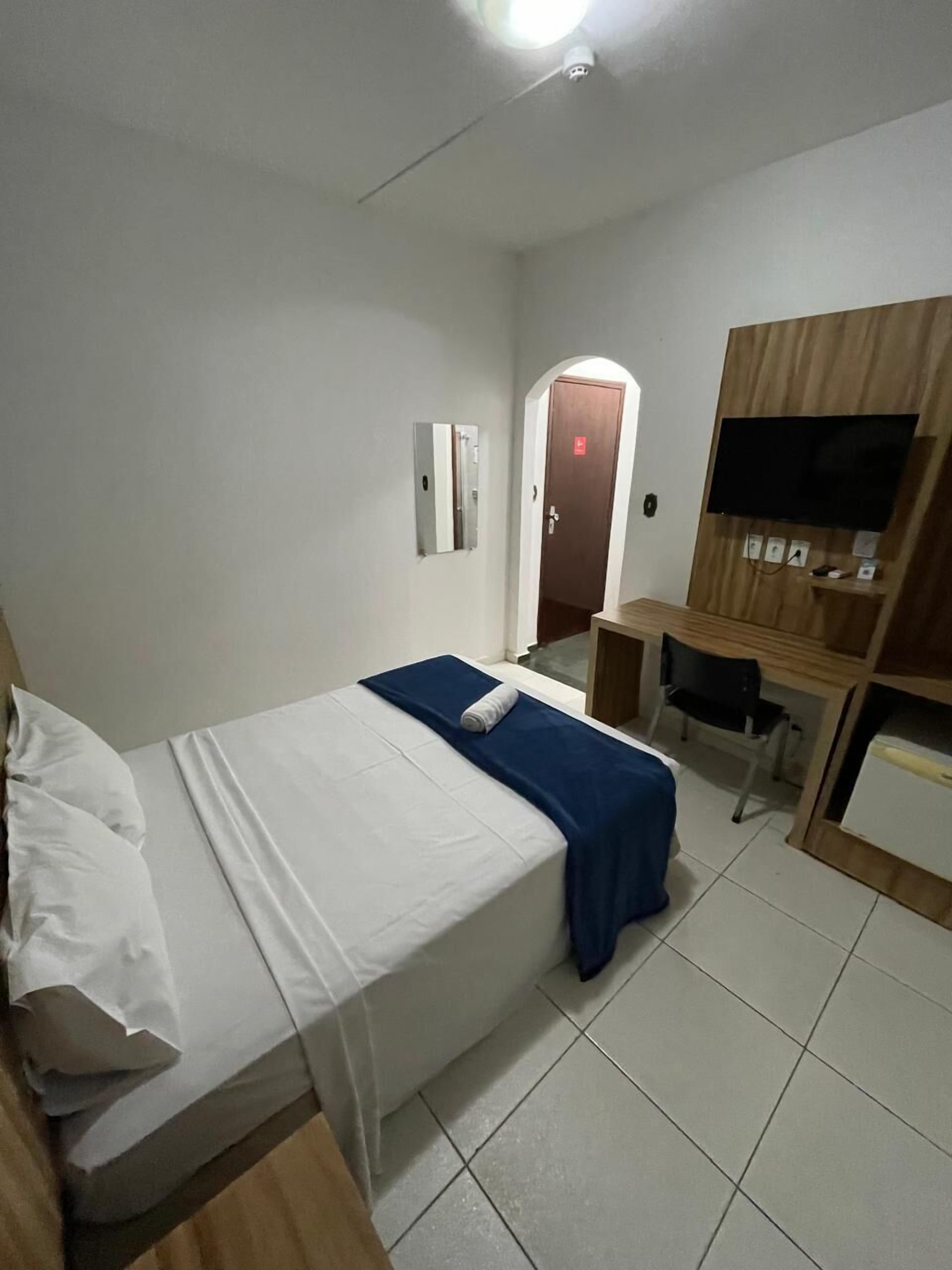 A hotel room with a bed, a desk, a television, and a door.
