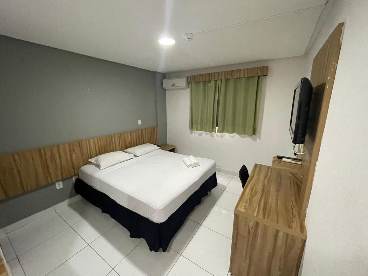 Habitación de hotel con cama, escritorio, silla, televisor y aire acondicionado.