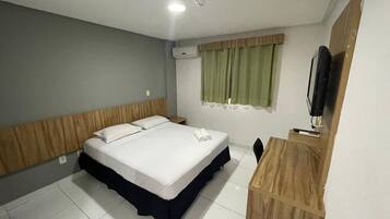 Habitación de hotel con cama, escritorio, silla, televisor y aire acondicionado.