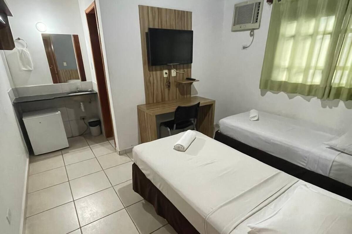 Une chambre d’hôtel comprenant un lit, un bureau avec une chaise, une télévision et une salle de bain avec un miroir et un lavabo.