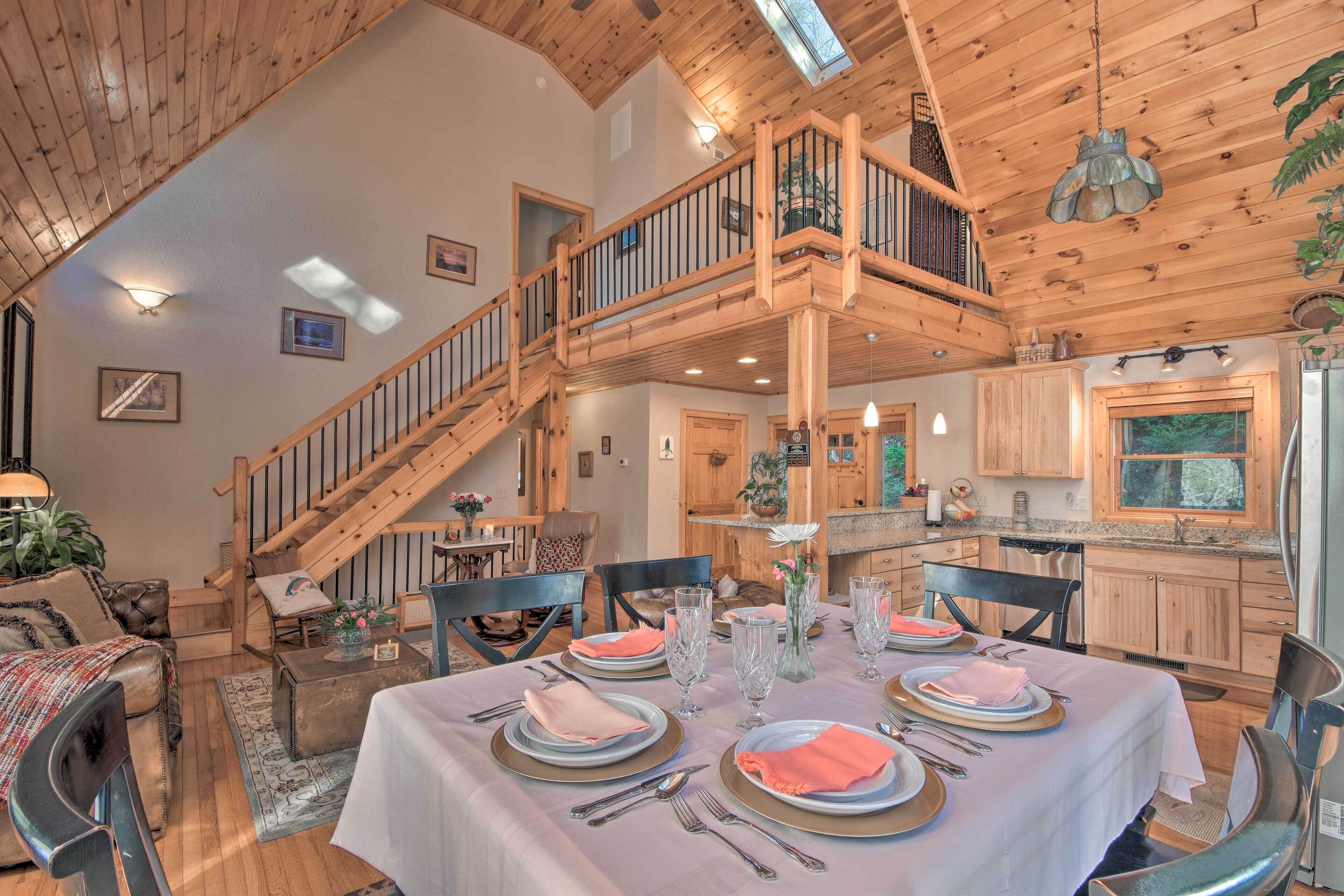 A spacious living area with a high ceiling, wooden staircase, and a dining table set for four.