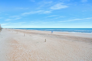 A wide, sandy beach with a clear blue sky and calm sea.