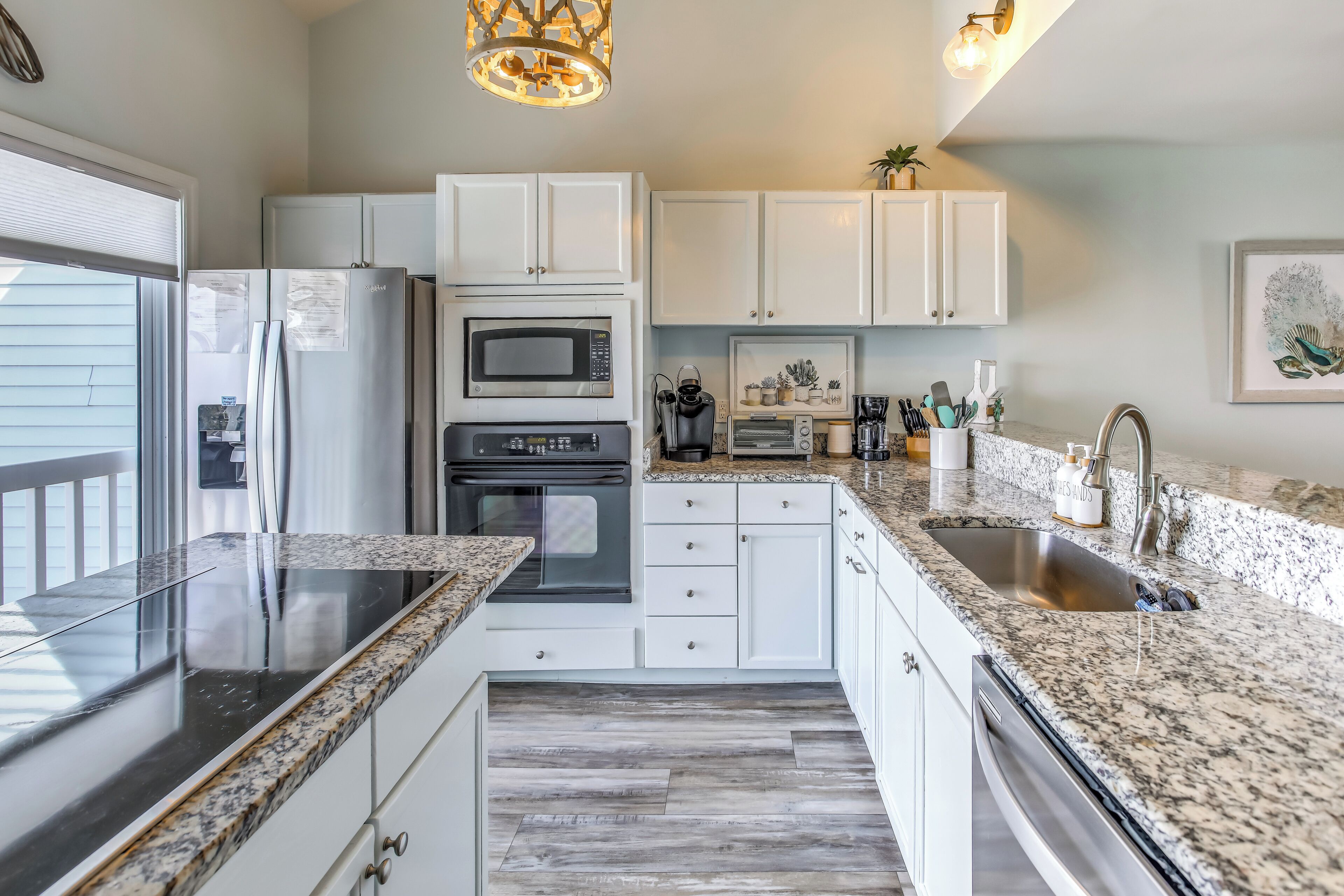 A modern kitchen with white cabinets, granite countertops, a stainless steel refrigerator, an oven, a microwave, and a sink.