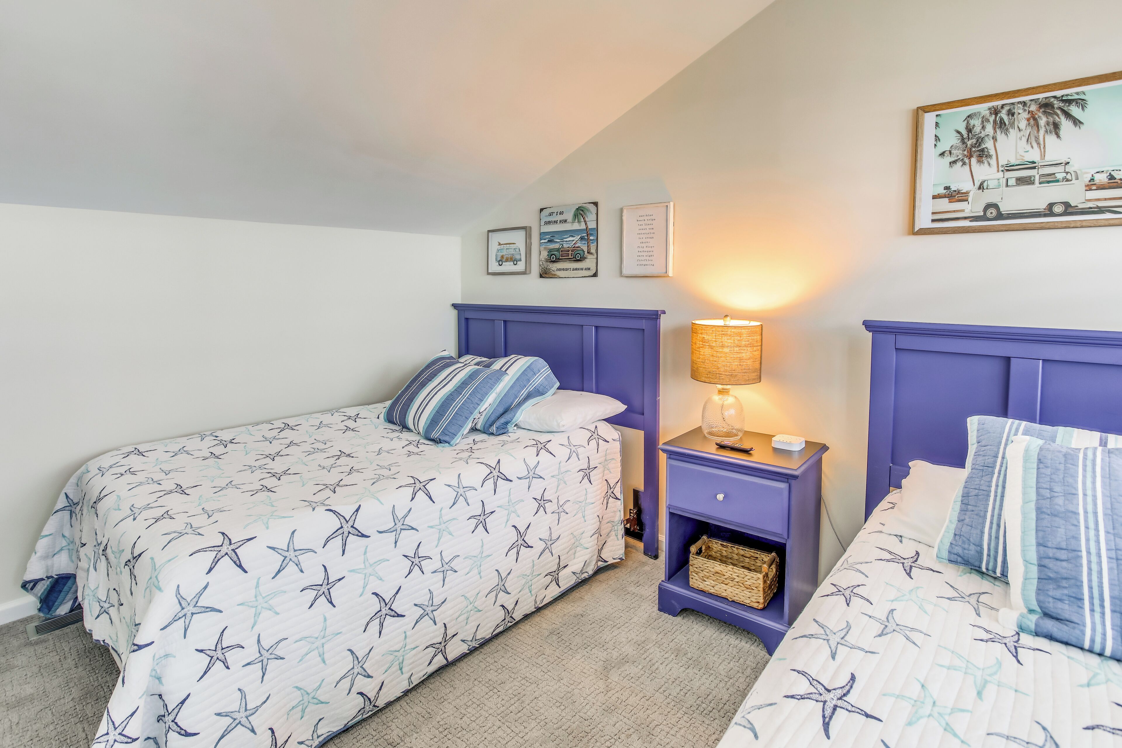 A bedroom with two beds, each with star-patterned bedding, a purple headboard, and a nightstand with a lamp.