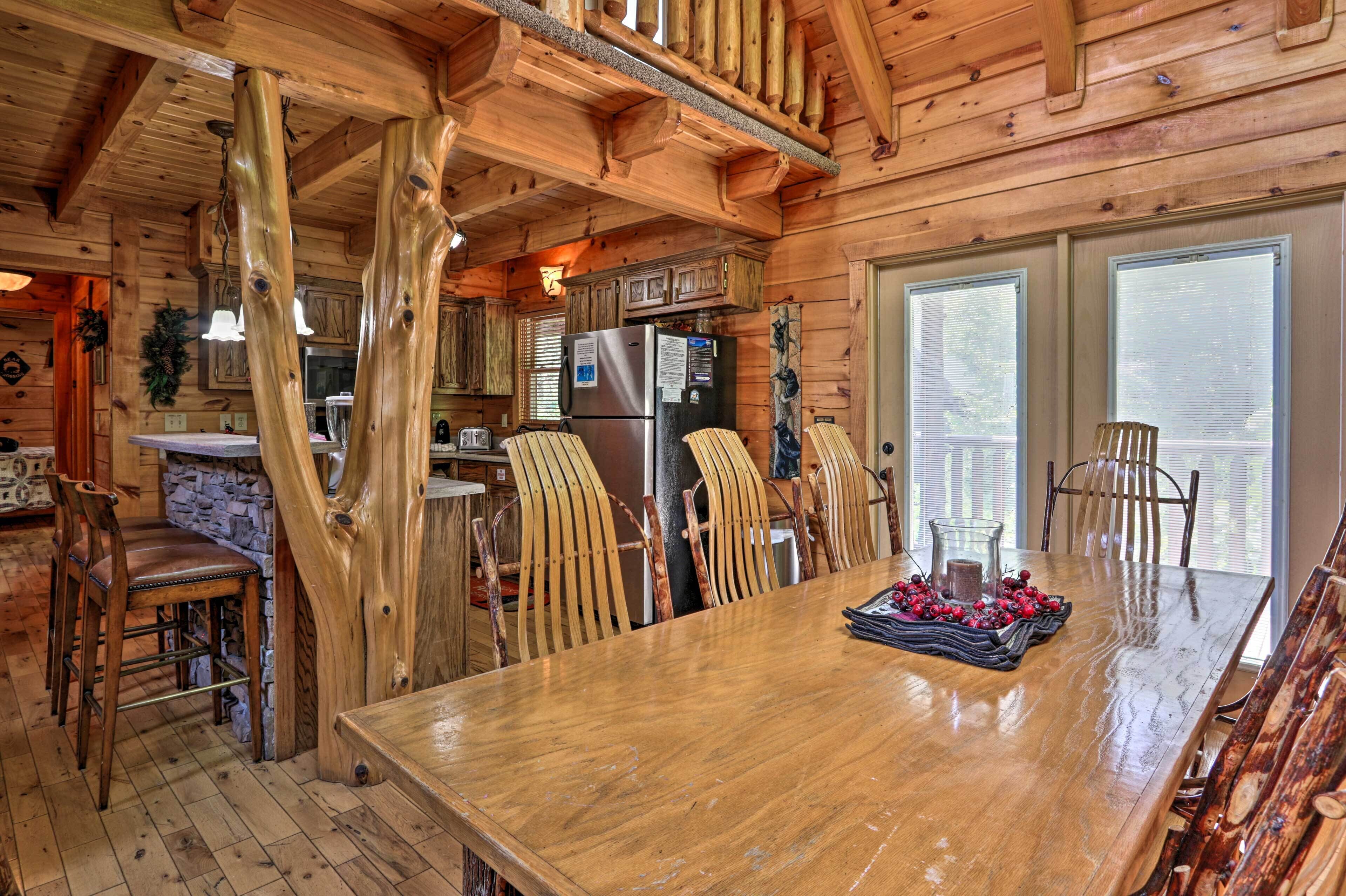 A wooden cabin interior with a dining area, kitchen, and a stone fireplace.