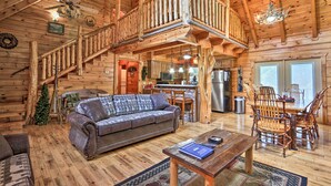 L’intérieur d’une cabane en rondins, avec un escalier en bois, un salon comprenant un canapé et une table basse, et un coin cuisine.